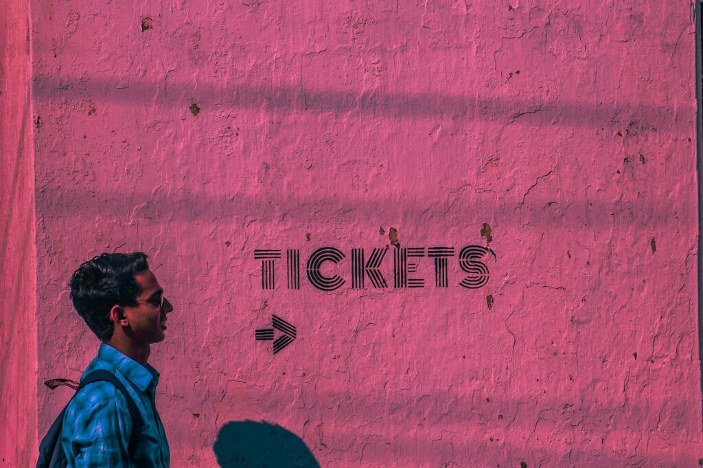 Profile view of a man walking past a textured pink wall with 'tickets' text and arrow.